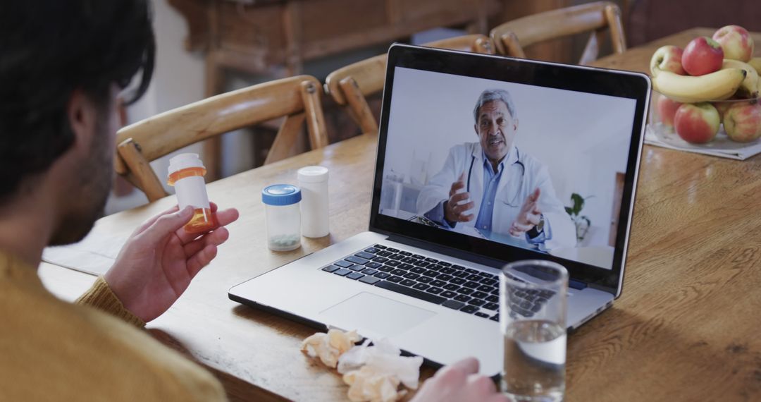 Caucasian man with pills on table having laptop video call with biracial male doctor at home - Free Images, Stock Photos and Pictures on Pikwizard.com