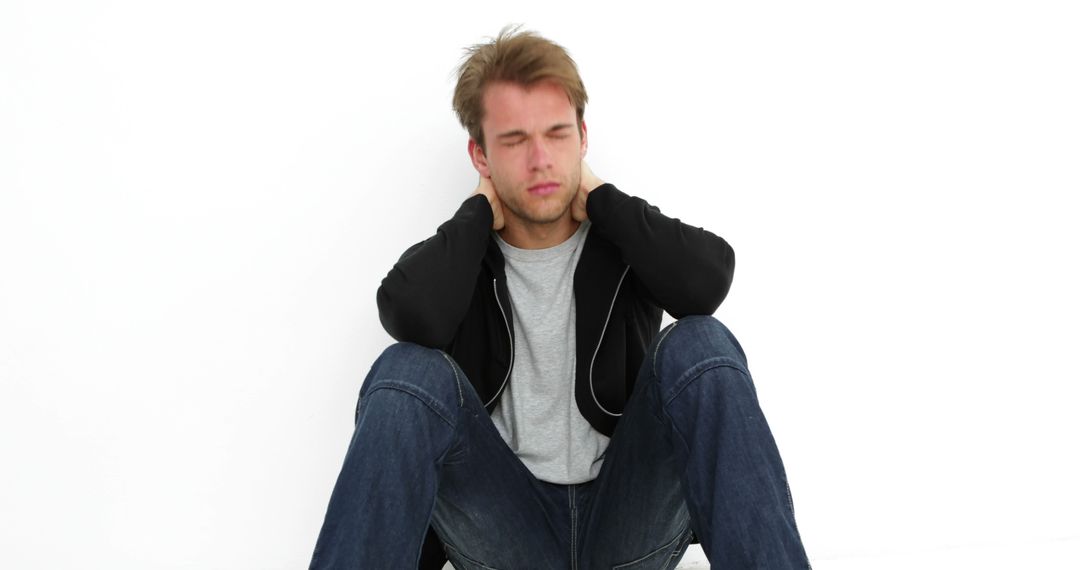 Young Man Sitting Against White Wall Holding Neck in Pain - Free Images, Stock Photos and Pictures on Pikwizard.com