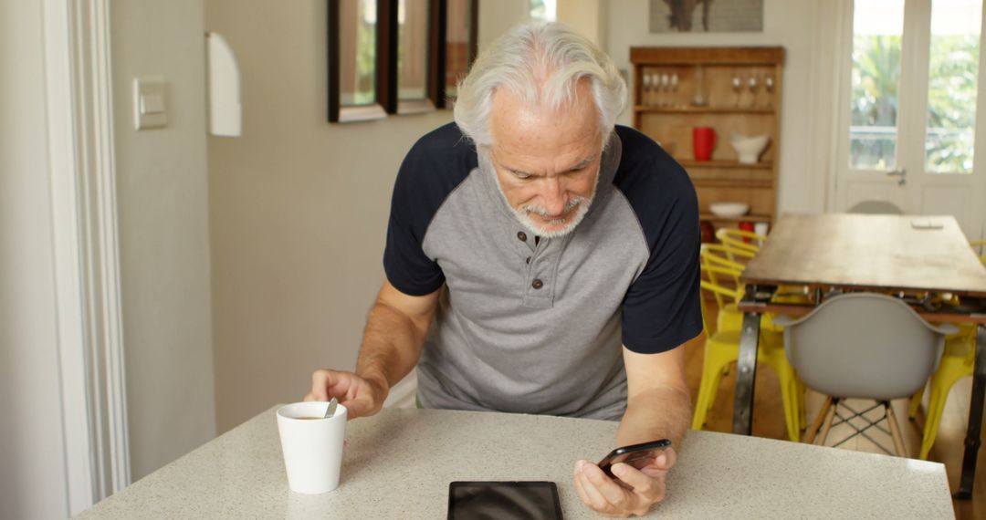 Senior Man in Kitchen Reading on Smartphone with Coffee - Free Images, Stock Photos and Pictures on Pikwizard.com