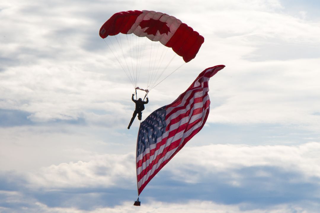 Skydiver Parachuting With Canadian and American Flags Against Cloudy Sky - Free Images, Stock Photos and Pictures on Pikwizard.com