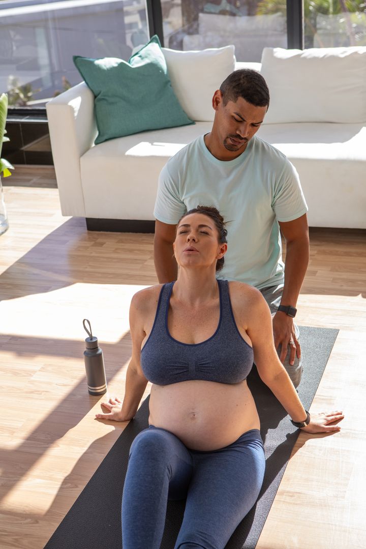 Pregnant Woman Stretching Supported by Partner in Relaxing Home Space
