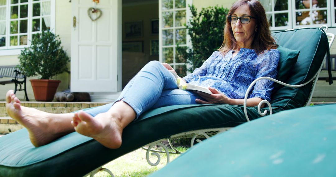 Relaxed Middle-Aged Woman Reading Book on Lounger in Sunlit Garden - Free Images, Stock Photos and Pictures on Pikwizard.com