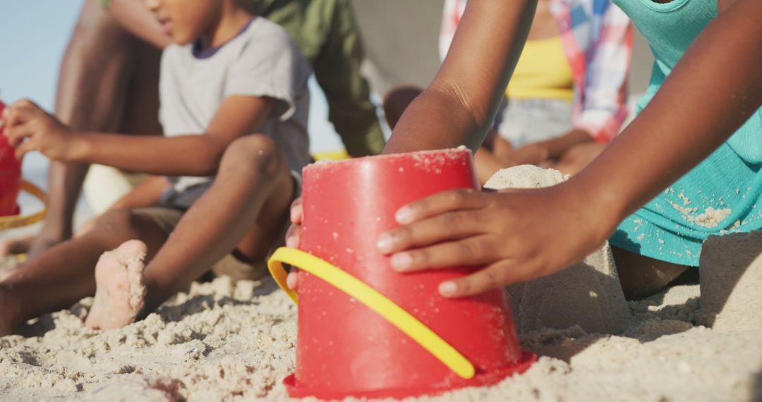 Children Building Sandcastles on Beach with Red Bucket - Free Images, Stock Photos and Pictures on Pikwizard.com