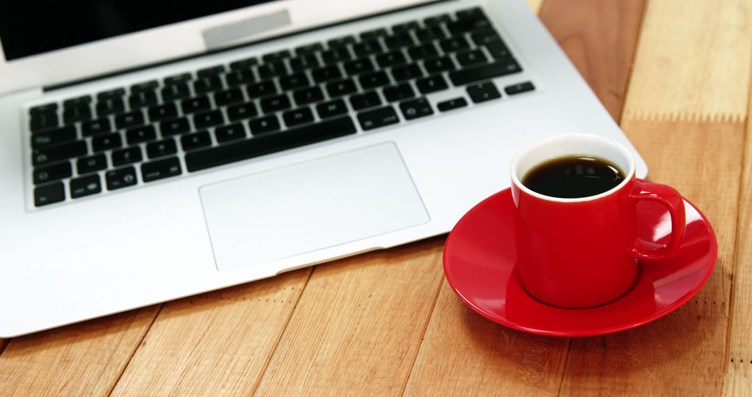 Red coffee cup next to laptop on wooden desk in office setting - Free Images, Stock Photos and Pictures on Pikwizard.com