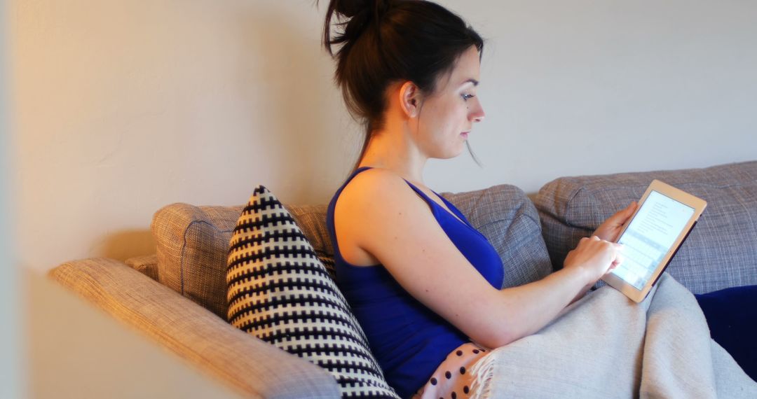 Woman Sitting on Couch with Tablet Reading in Cozy Living Room - Free Images, Stock Photos and Pictures on Pikwizard.com