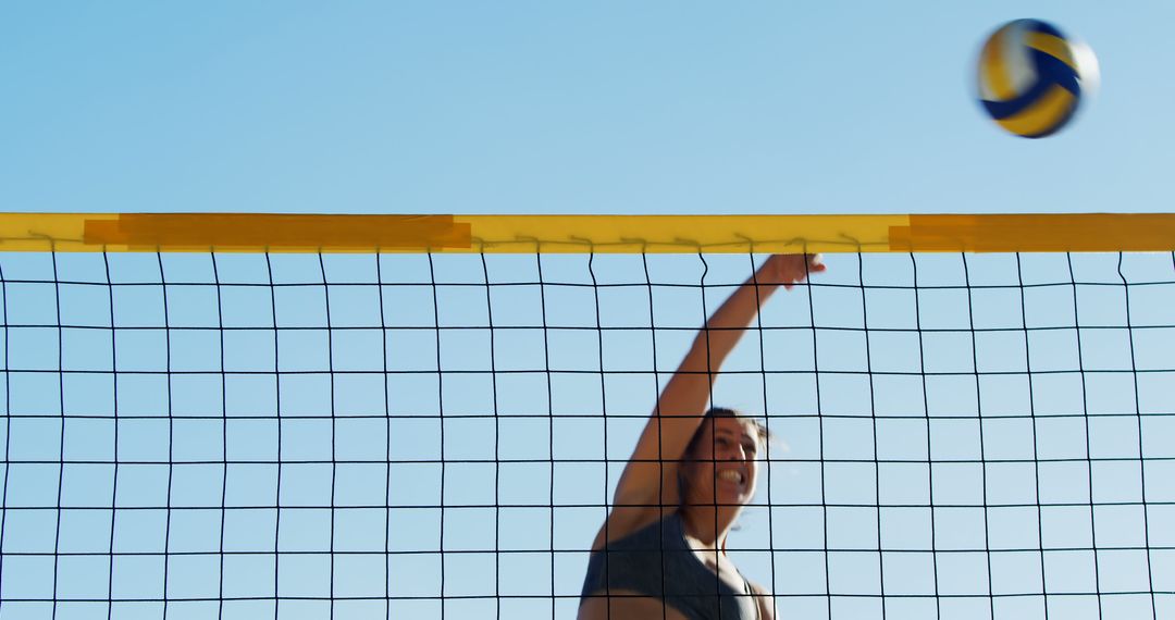 Active Woman Spiking Volleyball Over Net on Sunny Beach - Free Images, Stock Photos and Pictures on Pikwizard.com