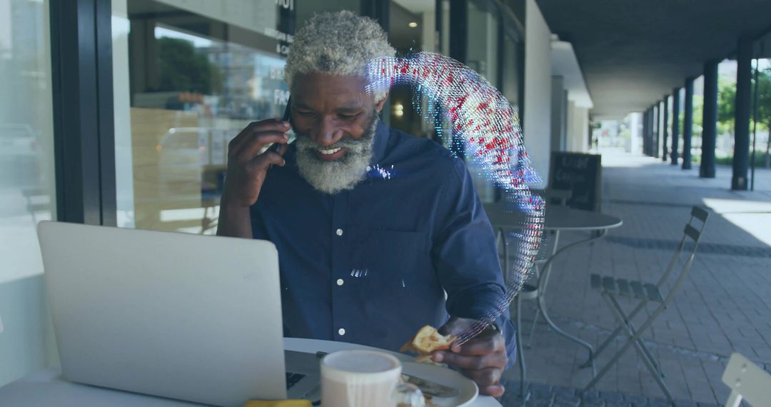 Man talking on smartphone while working on laptop and eating pastry at sidewalk cafe