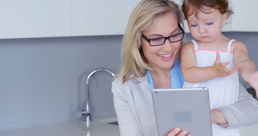 Smiling Businesswoman Holding Toddler and Tablet in Kitchen - Free Images, Stock Photos and Pictures on Pikwizard.com