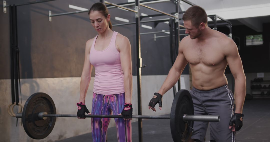 Woman Lifting Weights Guided by Shirtless Trainer in Gym