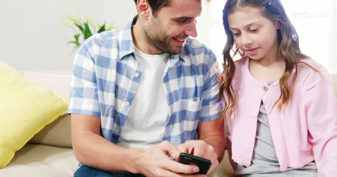 Father and Daughter Using Smartphone Together at Home on Couch - Free Images, Stock Photos and Pictures on Pikwizard.com