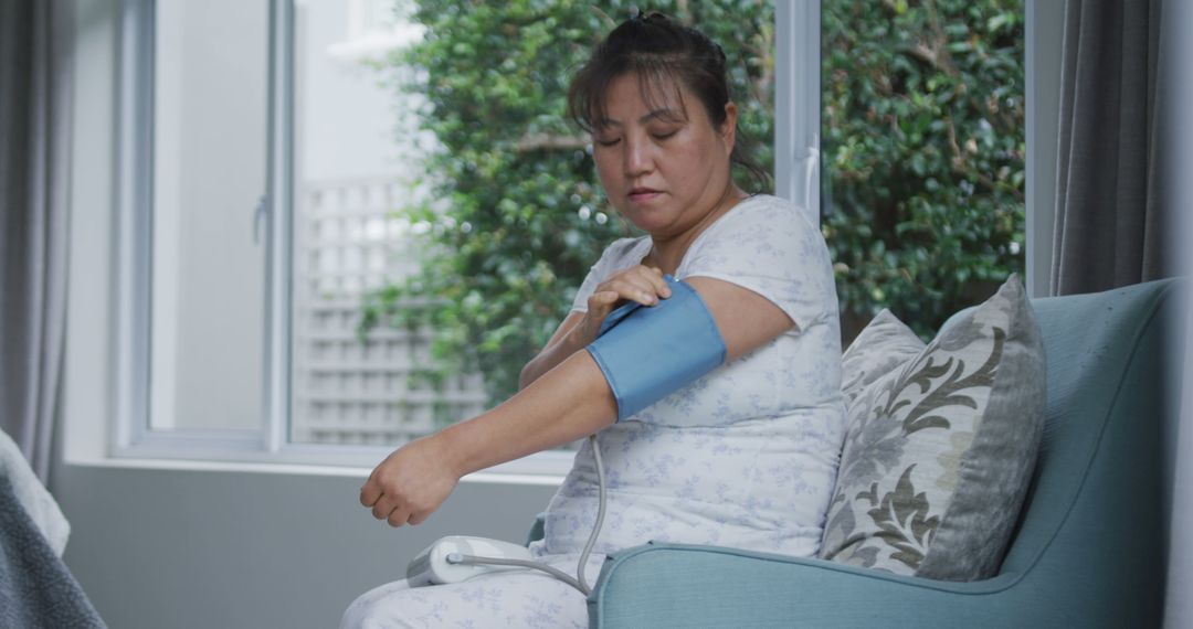 Asian woman using blood pressure monitor sitting on couch at home - Free Images, Stock Photos and Pictures on Pikwizard.com