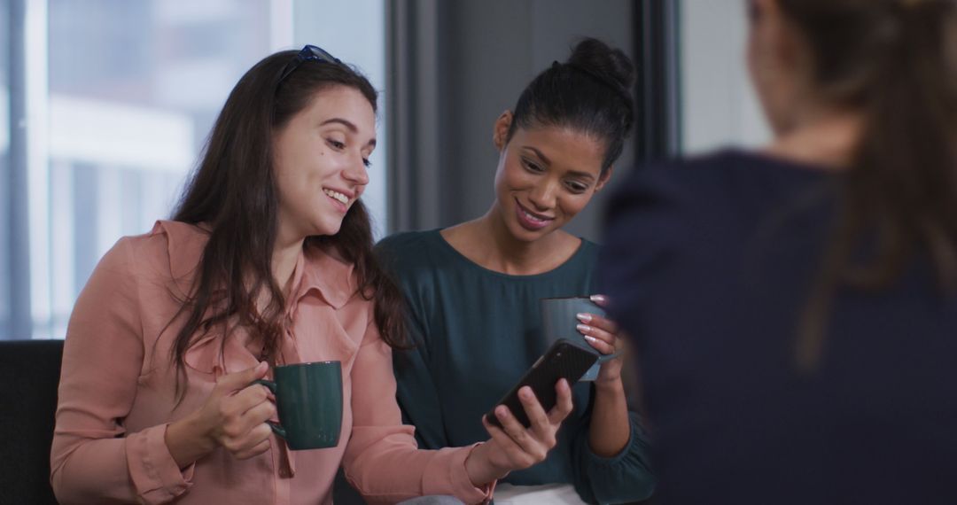 Diverse Young Women Smiling and Looking at Smartphone in Office - Free Images, Stock Photos and Pictures on Pikwizard.com