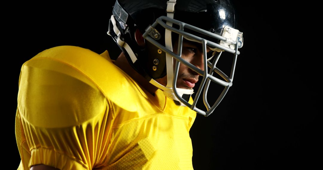 Focused Football Player in Yellow Jersey Wearing Helmet Lit Dramatically - Free Images, Stock Photos and Pictures on Pikwizard.com