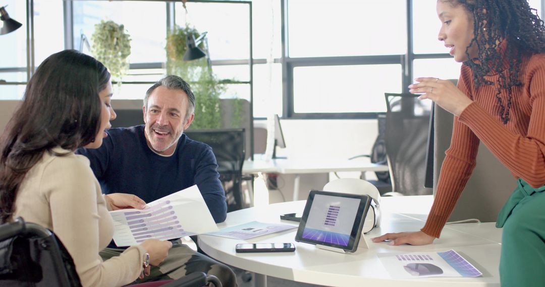 Inclusive Team Collaborating Around Round Table with Wheelchair User Reviewing Data Charts