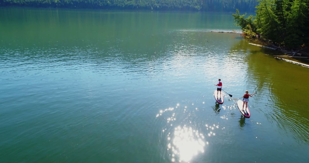 Paddleboarders on Serene Lake with Sunlight Reflections - Free Images, Stock Photos and Pictures on Pikwizard.com