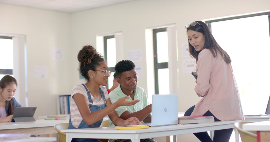 Engaged High School Students Collaborating with Teacher on Laptop