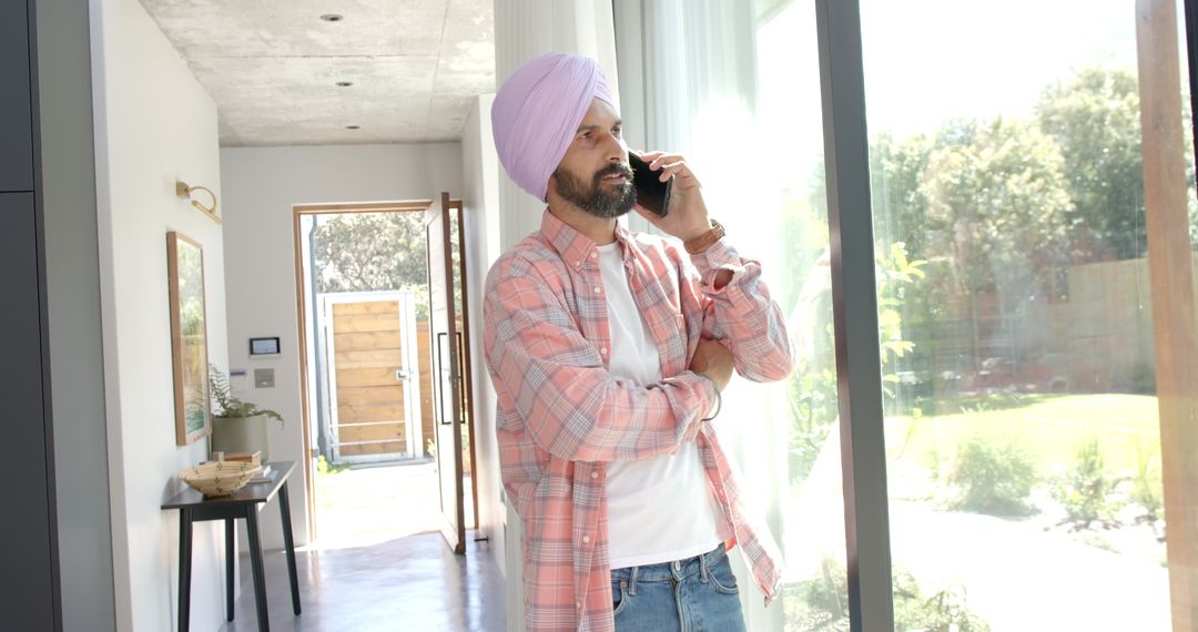 Man in Pink Turban Talking on Smartphone by Window at Home