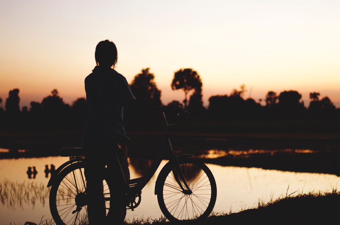 Silhouette of Person with Bicycle at Sunset by a Tranquil Lake - Free Images, Stock Photos and Pictures on Pikwizard.com