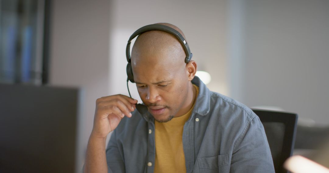 African American man adjusting headset while working at desk with monitor, focused