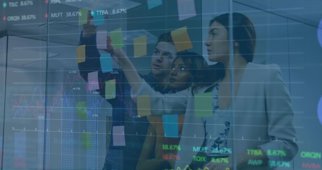 Collaborating team placing sticky notes on glass wall with financial charts overlay