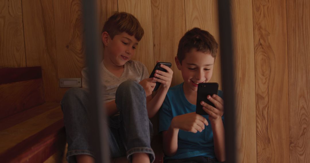 Two Boys Chatting and Playing on Smartphones Indoors - Free Images, Stock Photos and Pictures on Pikwizard.com