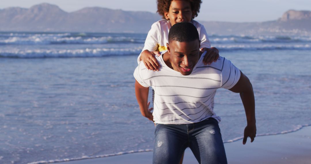 African american father giving a piggyback ride to his son at the beach - Free Images, Stock Photos and Pictures on Pikwizard.com