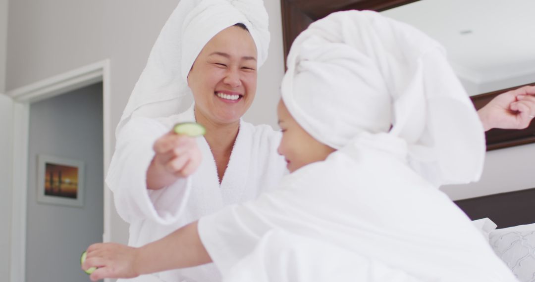 Image of happy asian mother and daughter in robes doing cucumber mask and having fun - Free Images, Stock Photos and Pictures on Pikwizard.com