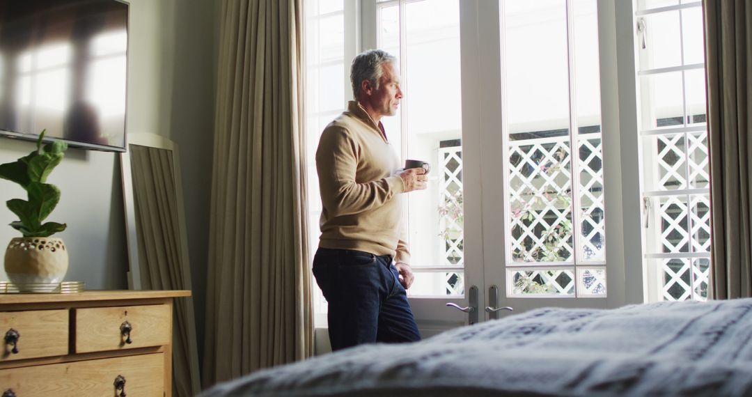 Middle-aged man enjoying morning coffee by window in cozy bedroom - Free Images, Stock Photos and Pictures on Pikwizard.com