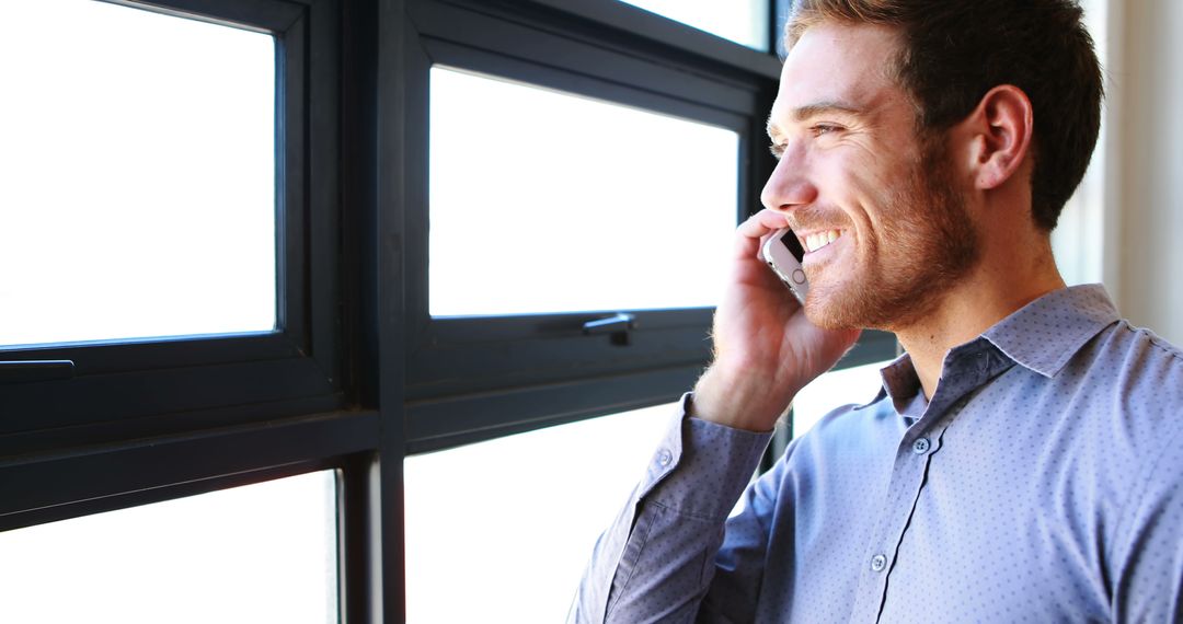 Smiling Businessman Talking on Smartphone by Window - Free Images, Stock Photos and Pictures on Pikwizard.com