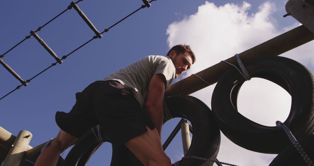 Man climbing obstacle course wall ropes under bright blue sky - Free Images, Stock Photos and Pictures on Pikwizard.com