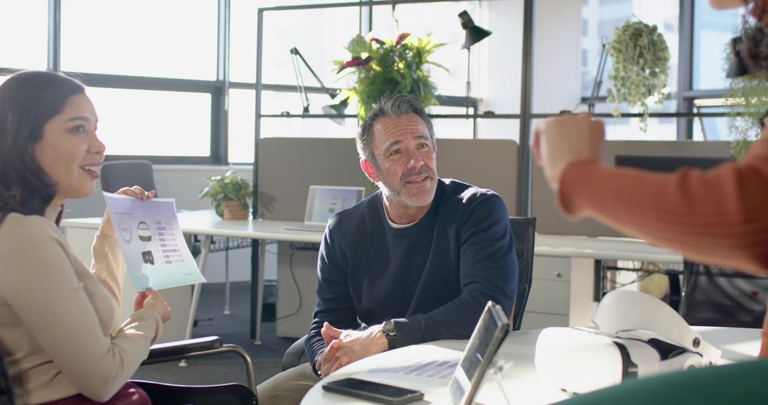 Multicultural team collaborating around round table in modern open-plan office with tablet and chart