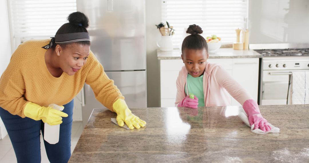 Happy biracial mother with daughter wearing rubber gloves and cleaning table in kitchen - Free Images, Stock Photos and Pictures on Pikwizard.com