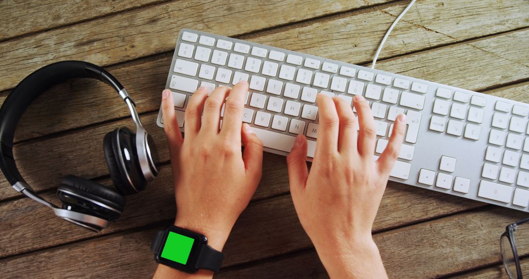 Hands Typing on Keyboard Wearing Smartwatch with Headphones Nearby - Free Images, Stock Photos and Pictures on Pikwizard.com