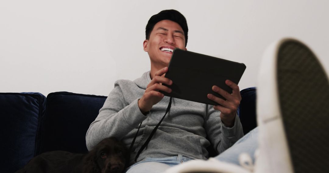 Young Man Relaxing on Sofa with Tablet and Dog at Home