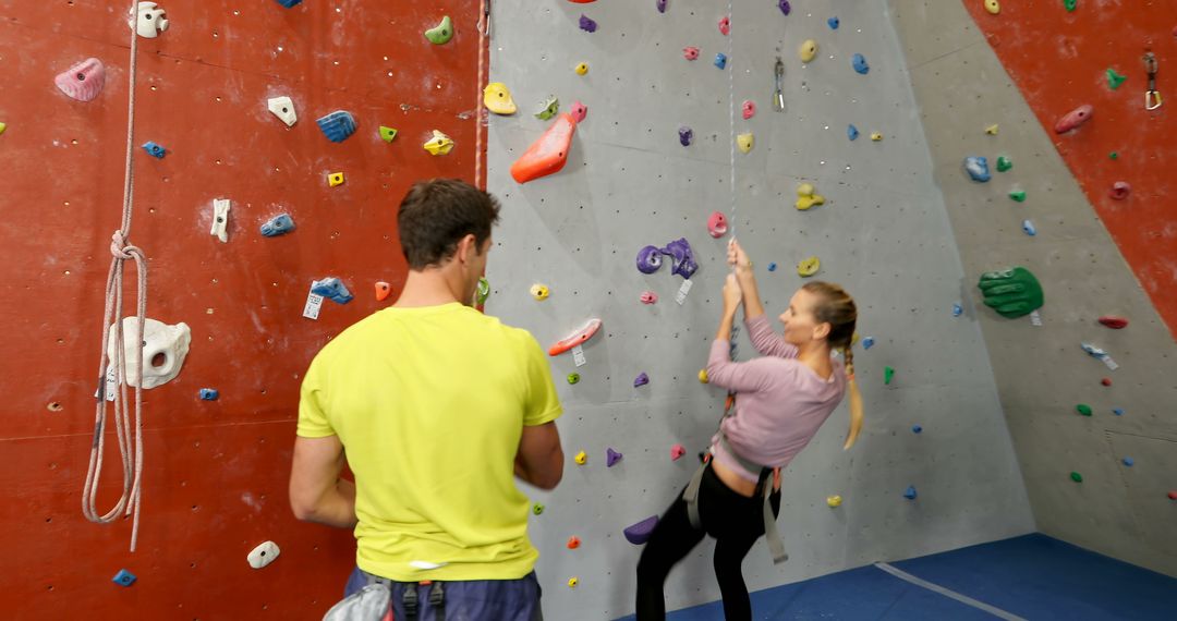 Young woman rock climbing while instructor assists at indoor climbing gym - Free Images, Stock Photos and Pictures on Pikwizard.com