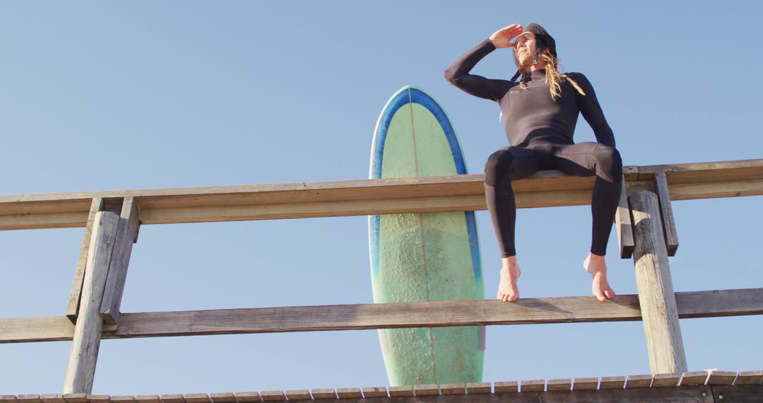 Female Surfer Sitting on Fence with Surfboard Enjoying Ocean View - Free Images, Stock Photos and Pictures on Pikwizard.com