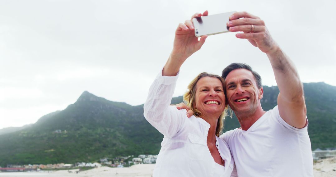 Couple Taking a Selfie on Beach with Mountains in Background - Free Images, Stock Photos and Pictures on Pikwizard.com