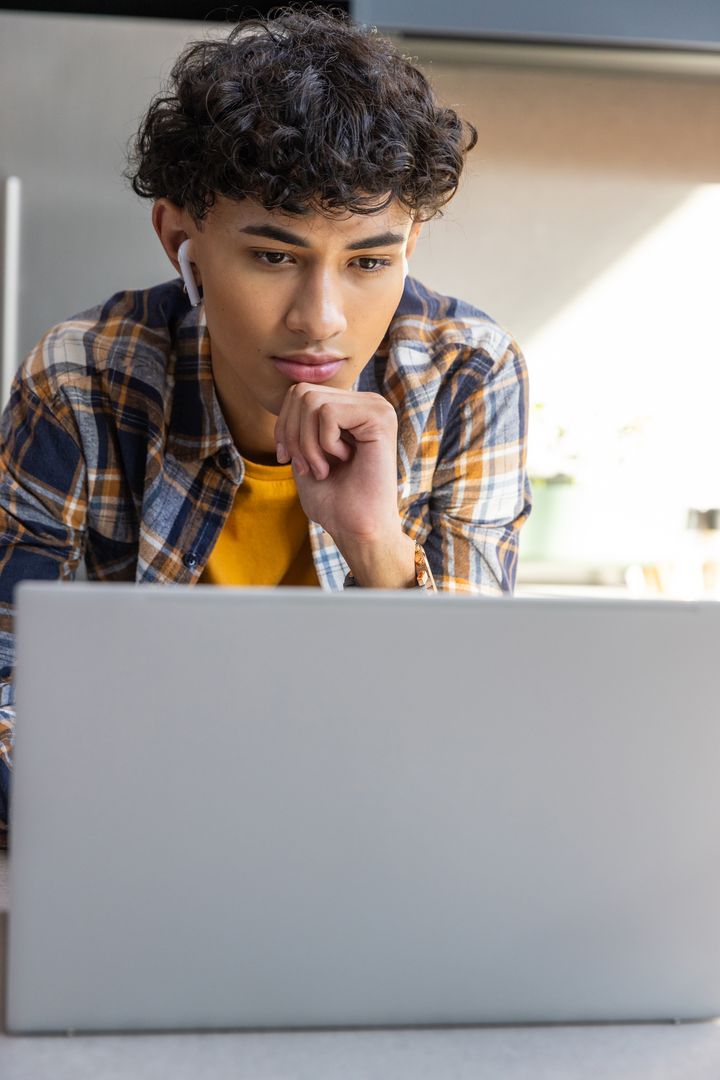 Young Man Concentrating on Laptop with Wireless Earbuds at Home