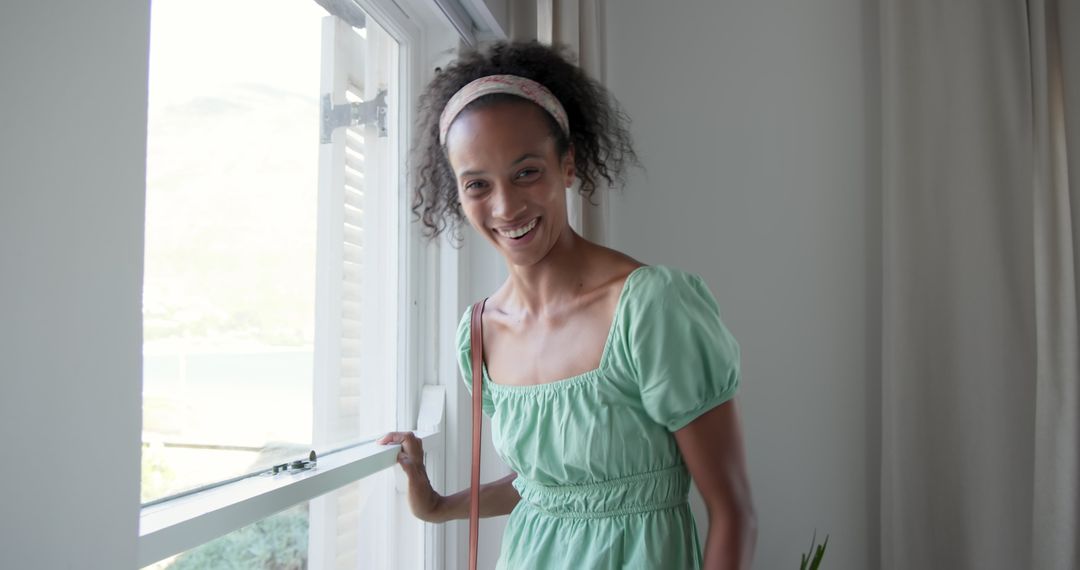 Smiling Woman in Light Green Dress by Window Embracing Sunlight