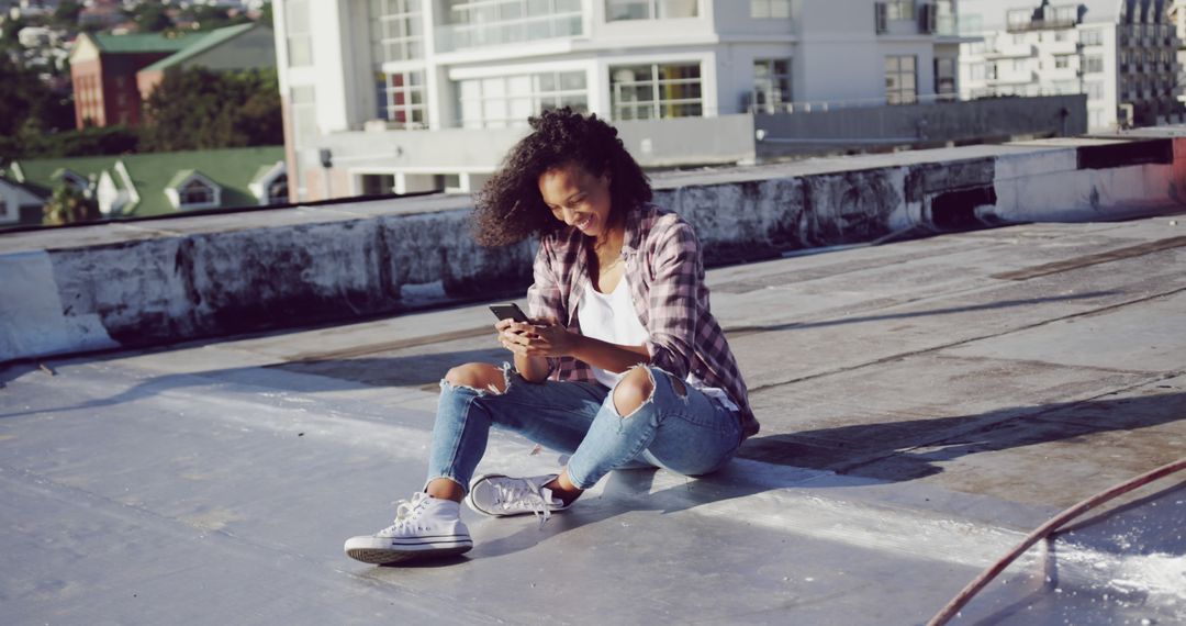 Young Woman Smiling While Using Smartphone on Rooftop - Free Images, Stock Photos and Pictures on Pikwizard.com