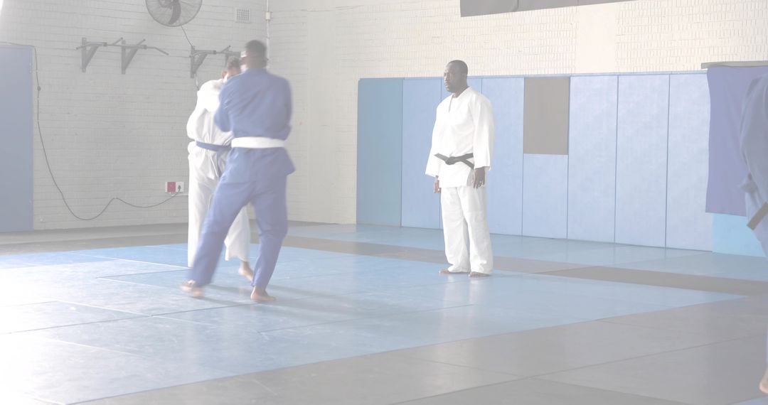 Martial arts instructor supervising judo sparring on tatami mats with students in gis