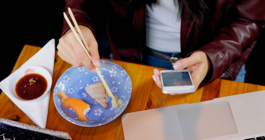 Young Person Eating Sushi with Chopsticks While Using Smartphone - Free Images, Stock Photos and Pictures on Pikwizard.com