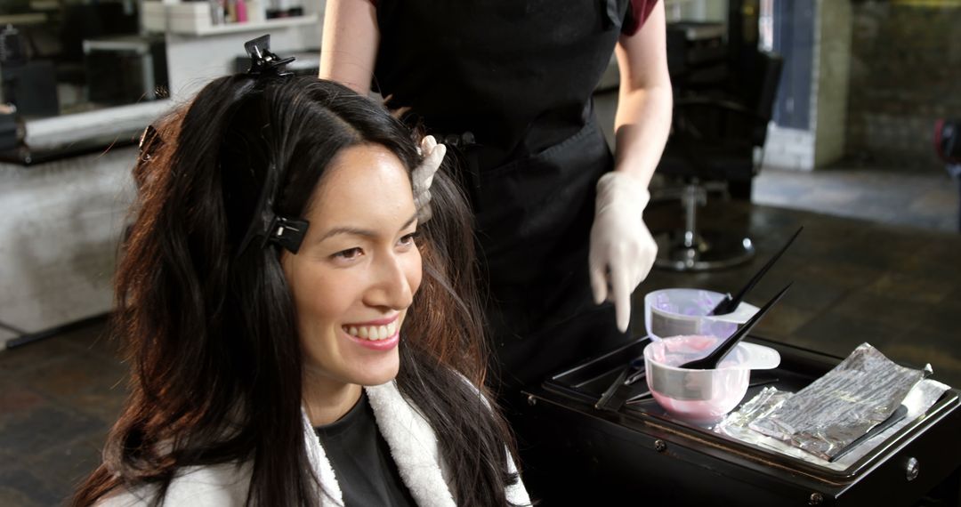 A young Asian woman smiles while getting her hair dyed at a salon, with copy space - Free Images, Stock Photos and Pictures on Pikwizard.com