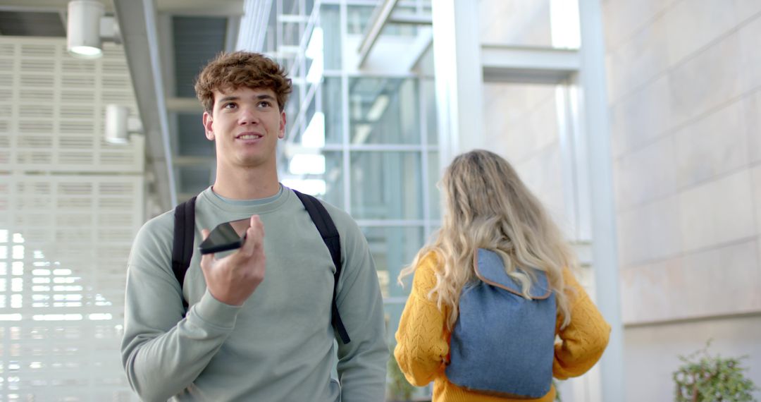 Male Student Speaking into Smartphone While Walking Through Modern Campus Atrium