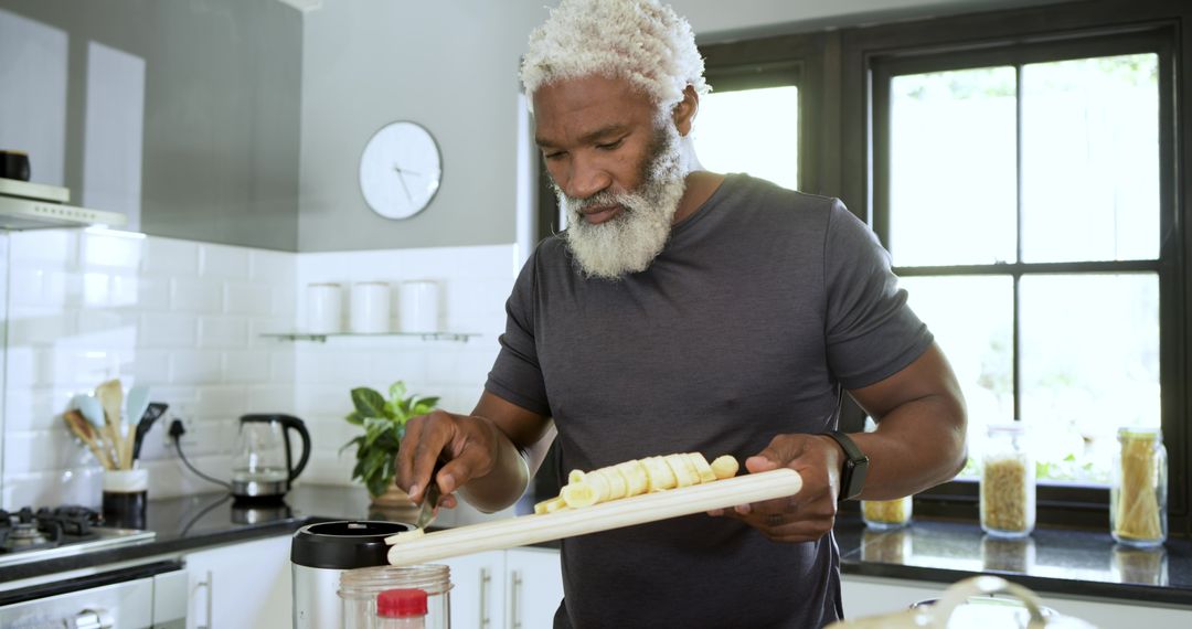 Senior Man Preparing Smoothie with Sliced Banana in Modern Kitchen