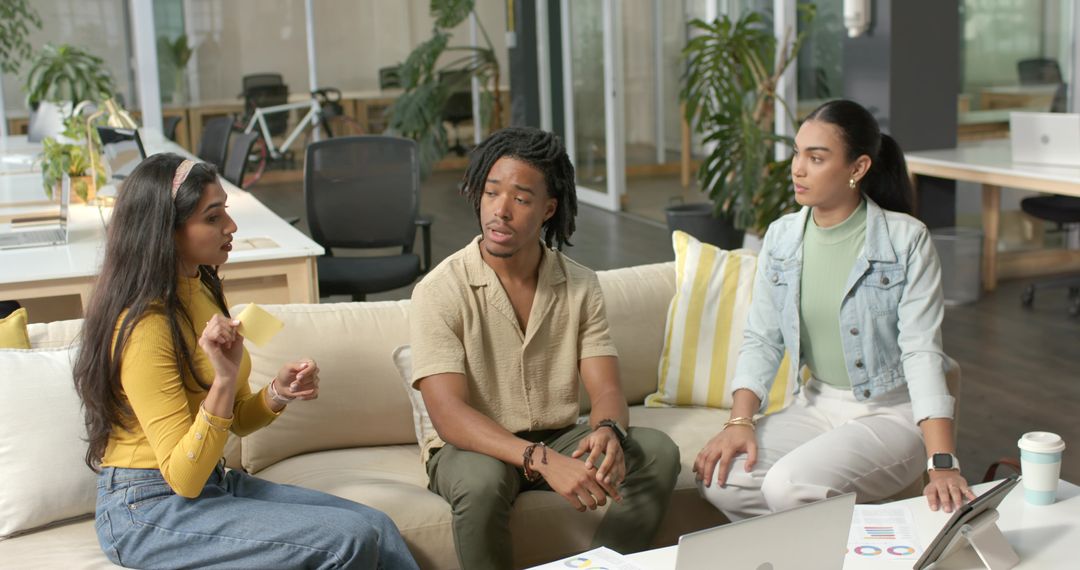 Diverse team collaborating and brainstorming on sofa with laptop in modern open-plan office