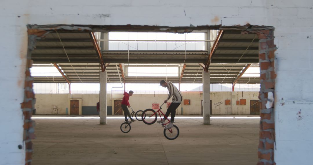 Two BMX cyclists practicing tricks in a spacious warehouse - Free Images, Stock Photos and Pictures on Pikwizard.com