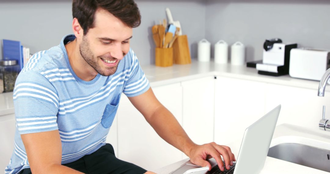 Young Man Smiling While Working at Home Using Laptop in Modern Kitchen - Free Images, Stock Photos and Pictures on Pikwizard.com