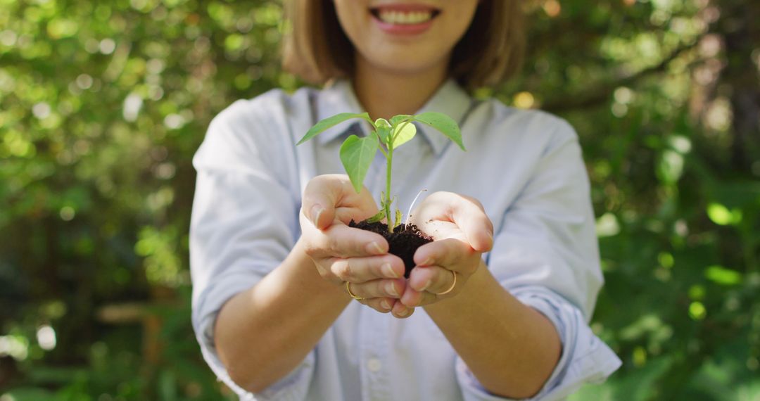 Asian woman holding plant in garden smiling on sunny day - Free Images, Stock Photos and Pictures on Pikwizard.com