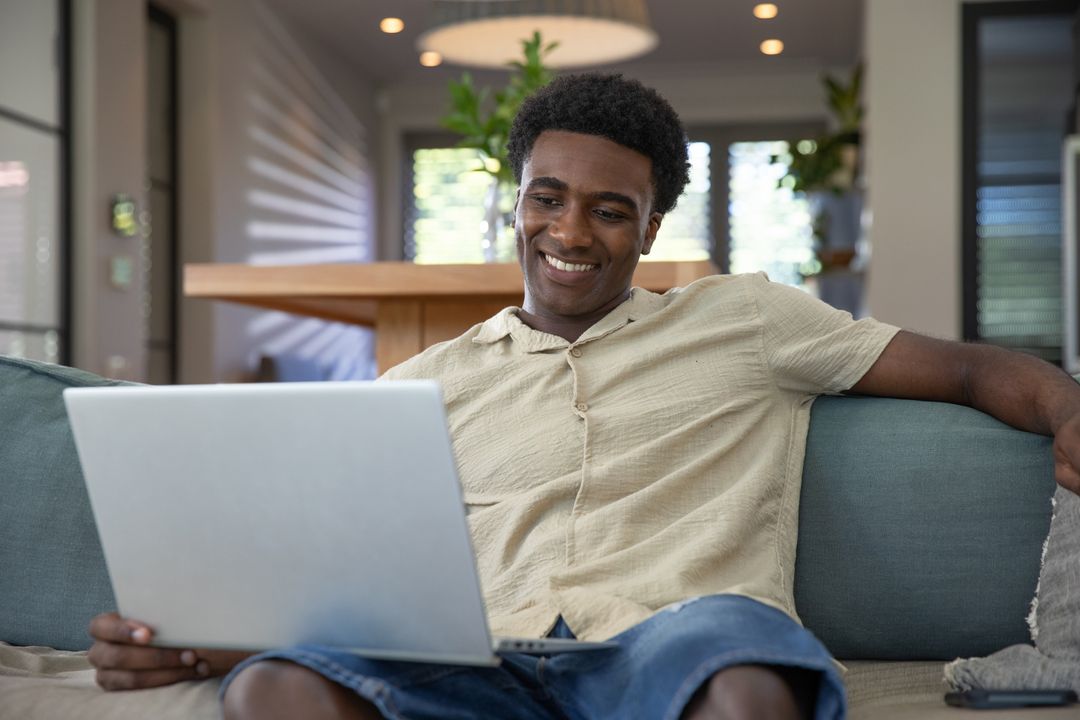 Man Smiling While Using Laptop on Sofa in Relaxed Living Room